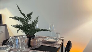 A dining table set with plates, glasses, and a pitcher, with a fern plant and a lamp in the background.
