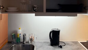 A kitchen with a stainless steel sink, a coffee maker, and shelves above containing various kitchenware.