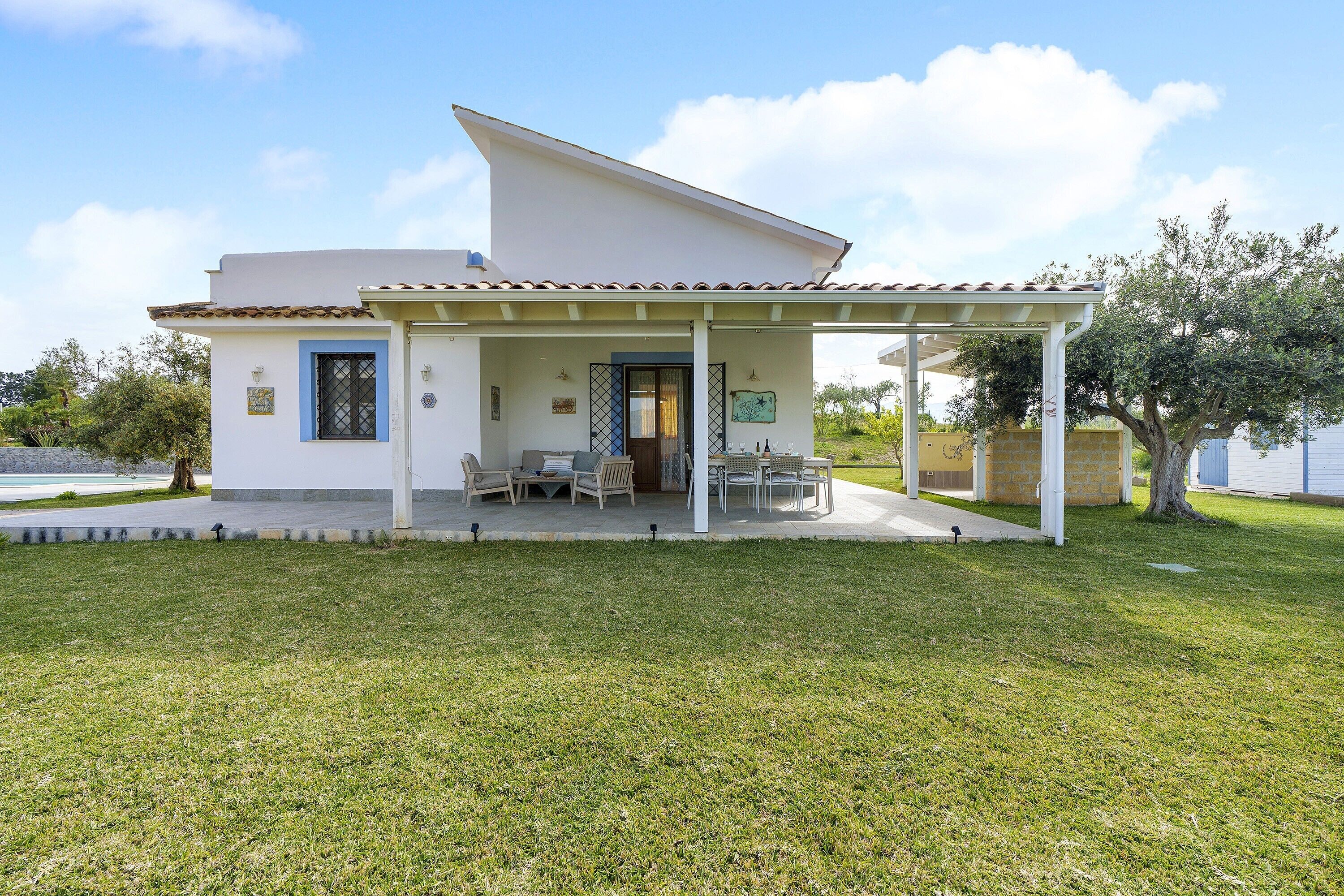 Ein einstöckiges Haus mit überdachter Terrasse, einem kleinen Garten und einer Tür mit Fenster.