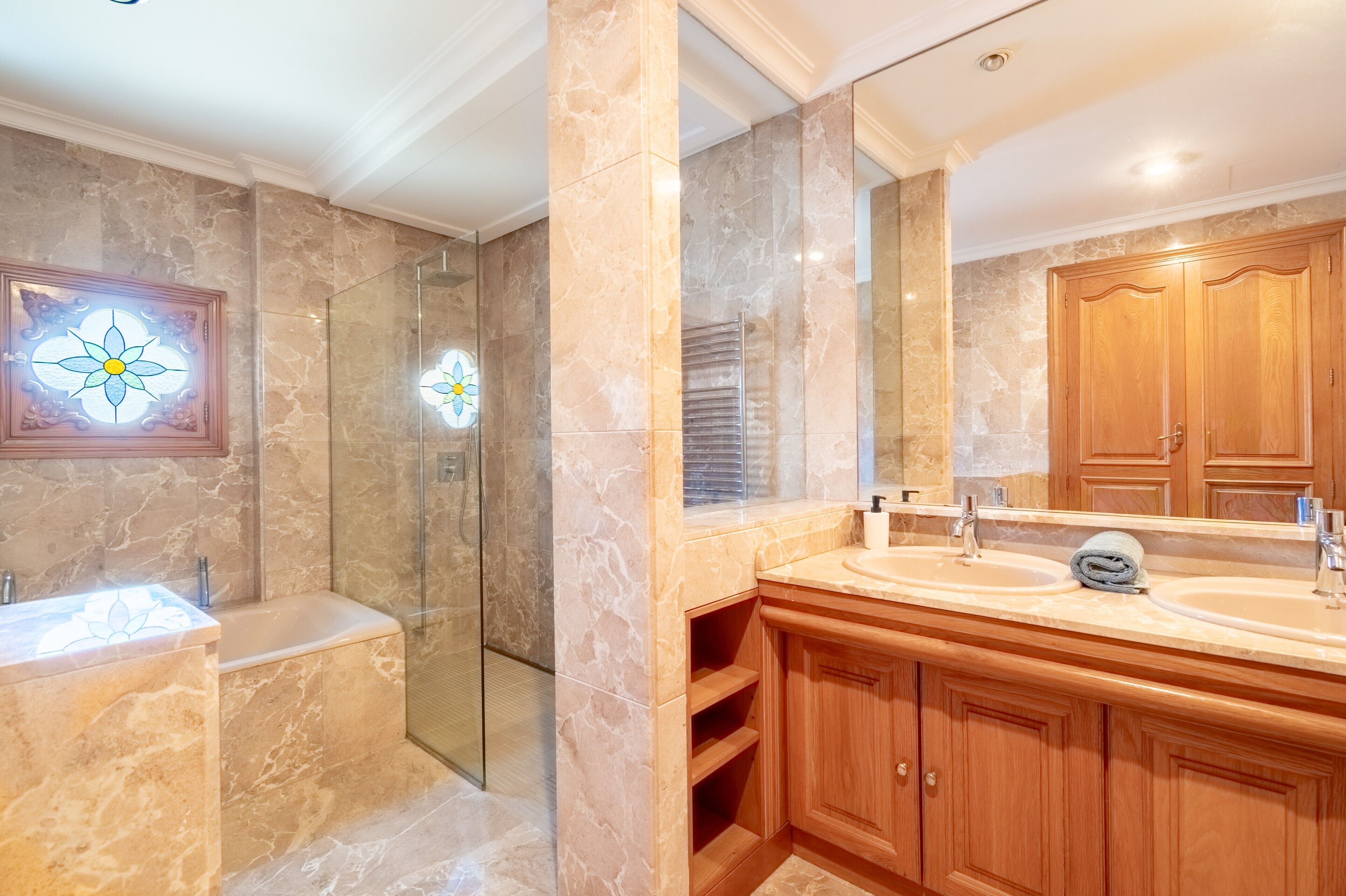 Un baño con paredes de mármol, cabina de ducha de vidrio, muebles de madera y un espejo grande.