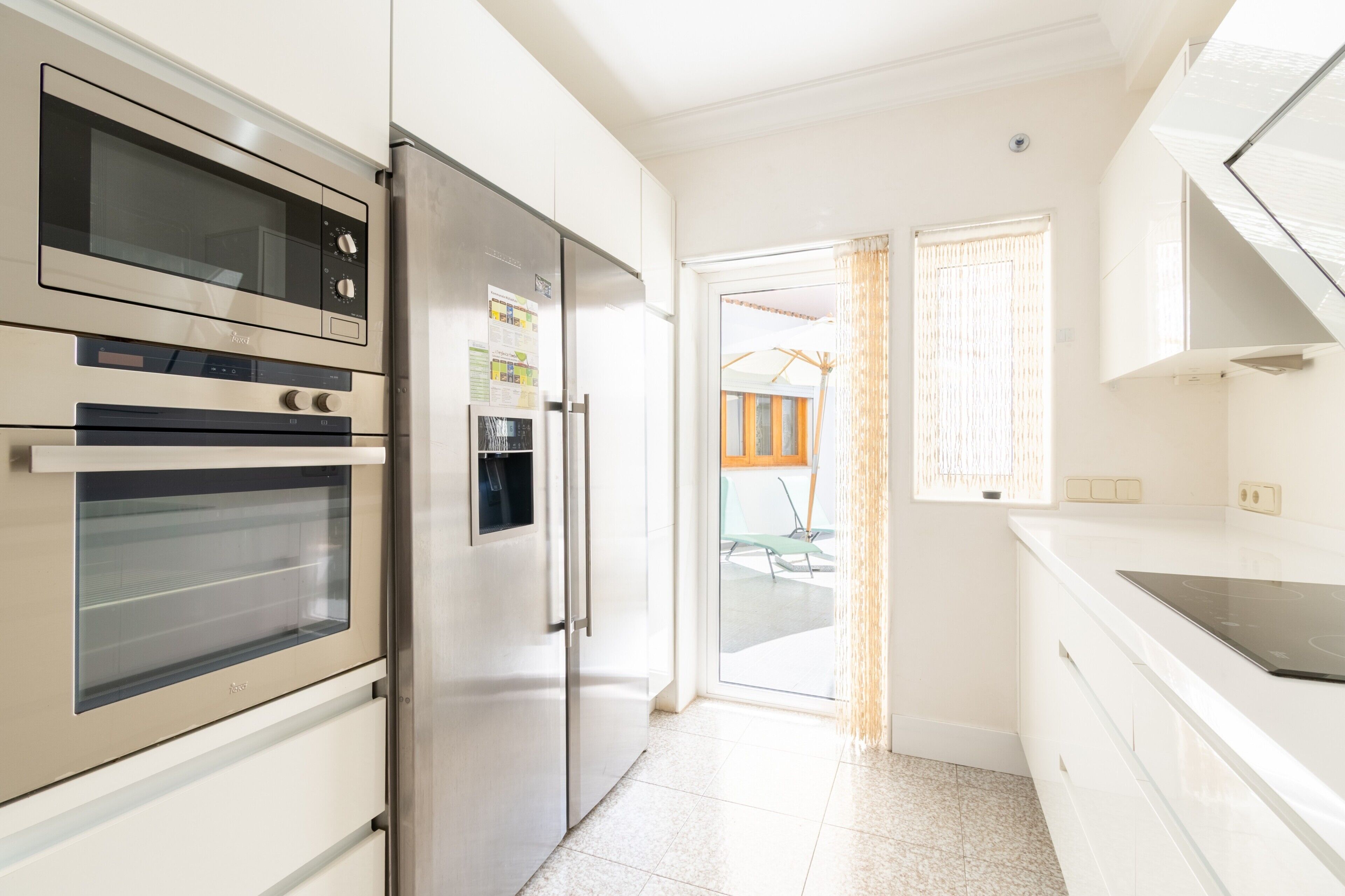 A modern kitchen with built-in appliances, a glass door refrigerator, and a view to the outside.