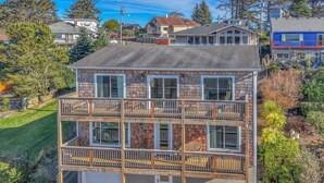 A two-story building with a balcony on the second floor, a garage at the base, and a landscaped yard. - Expansive Decks, Two Living Areas with Fireplaces! (Lincoln City)