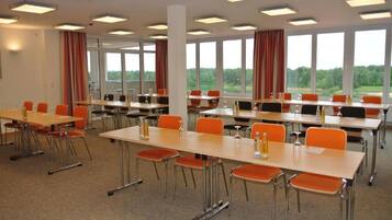 A conference room with multiple tables and chairs, large windows, and ceiling lights.
