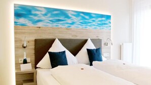 Habitación de hotel con cabecera de madera, cama con ropa de cama blanca y una obra de arte en la pared que representa un cielo azul.