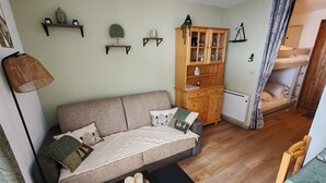 Un salon chaleureux avec un canapé, un meuble, une petite table avec des bougies et, au fond, un lit superposé.