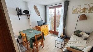 Un salon chaleureux avec une table en bois, des chaises, un canapé, un téléviseur et une fenêtre donnant sur des arbres.