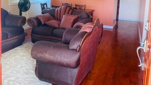Un salon spacieux avec un grand canapé d’angle, une table à manger et un ventilateur.
