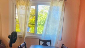 Un coin repas avec une table et des chaises, une fenêtre avec des rideaux et un ventilateur de plafond.