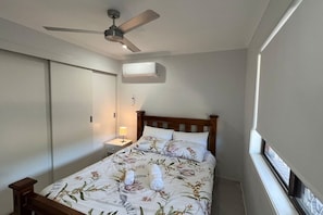 Un dormitori amb un llit, una tauleta de nit, un ventilador de sostre, un aparell d'aire condicionat i una finestra.