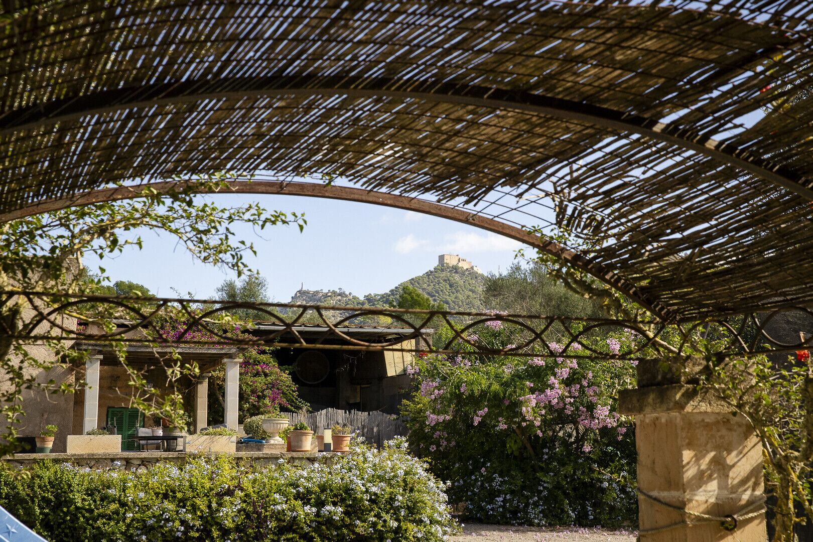 Un'area esterna riparata con una struttura in pietra, piante in vaso e vista su una collina con un edificio simile a un castello.