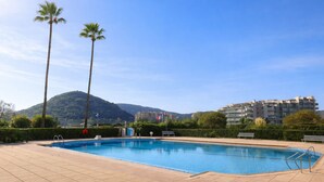 A swimming pool with a tiled deck, benches, and palm trees. - Le Masters Golf and Sea (Mandelieu-la-Napoule)