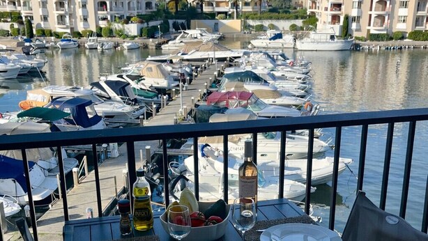 A dining table set with plates, glasses, and a bowl of fruit on a balcony overlooking a marina with boats and buildings in the background. - Le Masters Golf and Sea (Mandelieu-la-Napoule)