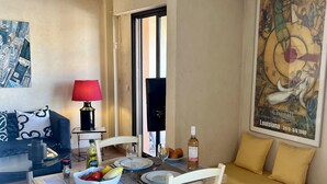 A dining area with a table set for two, a sofa, a painting, and a television. - Le Masters Golf and Sea (Mandelieu-la-Napoule)