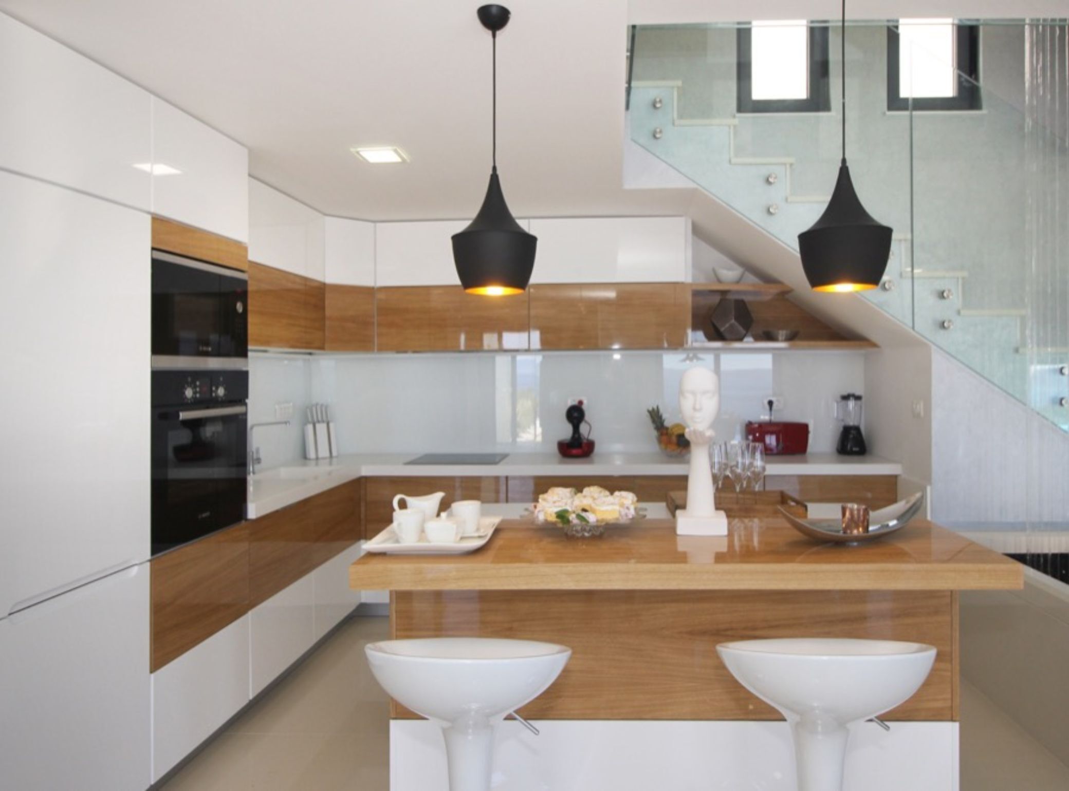 Een moderne keuken met witte kastjes, houten werkbladen en zwarte hanglampen.
