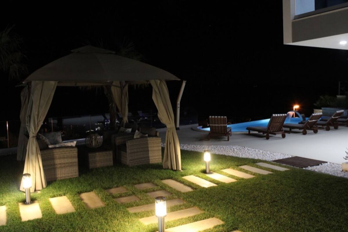 A nighttime outdoor seating area with a gazebo, lounge chairs, and a pool.