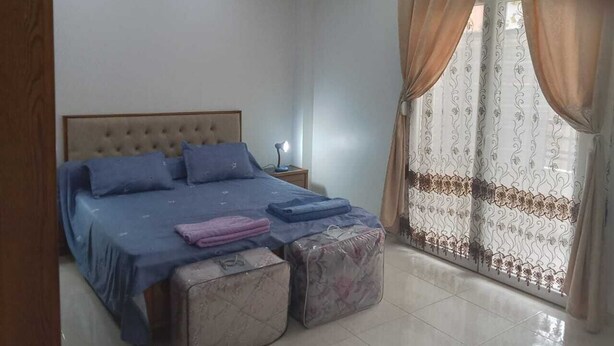 Un dormitorio con cama, mesita de noche, cortinas y ventana.