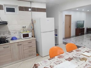 Eine Küche mit Mikrowelle, Herd und Kühlschrank. Ein Esstisch mit Stühlen steht bereit.