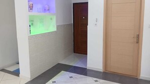 Un pasillo con piso de baldosas, una puerta de madera y un estante fijado a la pared con objetos decorativos.