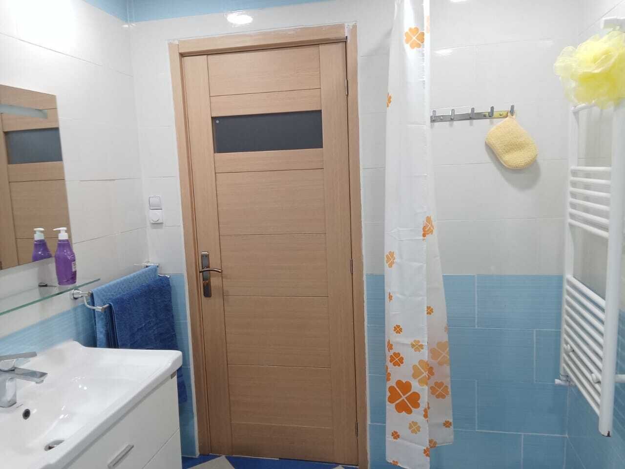 A bathroom with a wooden door, a white sink, a blue towel, and a shower curtain with a floral pattern.