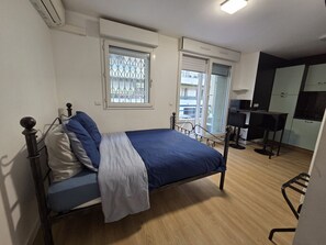 A bedroom with a bed, a desk, and a chair, with windows and an air conditioning unit. - Aya`s Studio with Balcony (Nice)