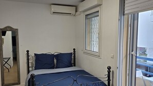 Un dormitorio con cama, aire acondicionado, ventana con persianas y un espejo.