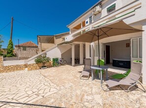 A covered outdoor area with a table and chairs, a hot tub, and a stone pathway leading to a building. - Holiday House Neven (Marina)