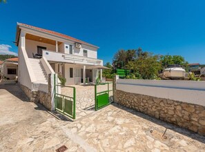 A two-story house with a stone facade, a tiled roof, and a green gate. - Holiday House Neven (Marina)