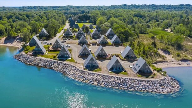 Ein Küstenresort mit mehreren kabinenartigen Häusern mit Kegeldächern, die um eine zentrale Straße angeordnet sind und durch einen steinigen Wellenbrecher verbunden werden.