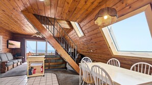 Un interior de madera con un comedor, una escalera y un ventanal grande.