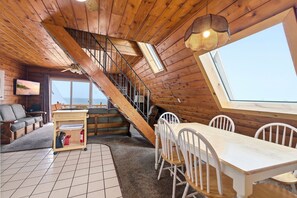 Un interior de madera con un comedor, una escalera y un ventanal grande.