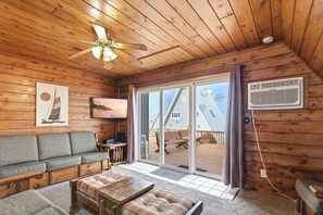 A wooden interior with a sofa, a table, a ceiling fan, and a sliding glass door leading to an outdoor deck.