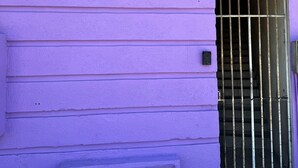 Ein violettes Gebäude mit vergittertem Fenster und einer kleinen Tür.
