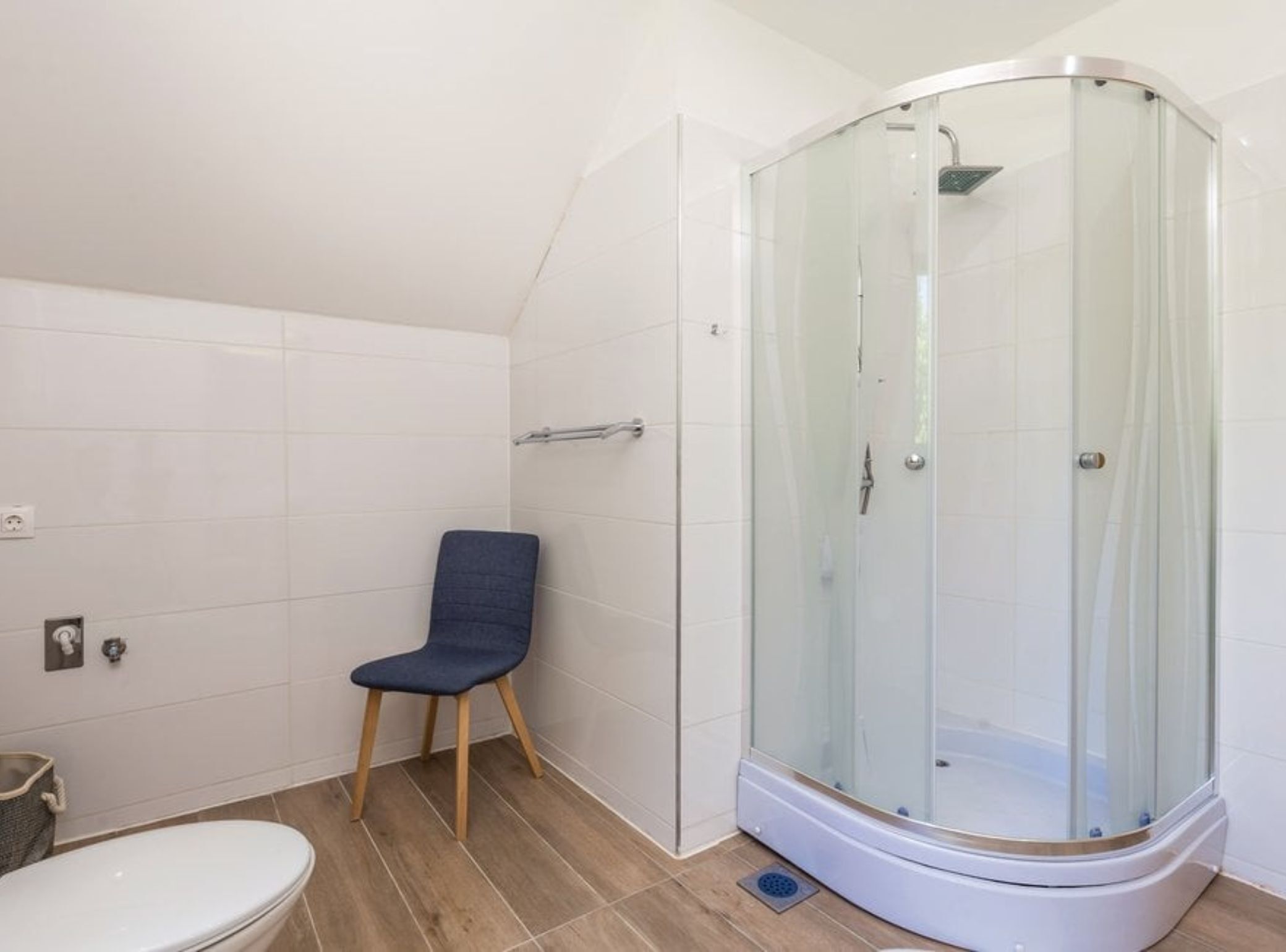 A modern bathroom with a glass-enclosed shower, a wooden chair, and a toilet.