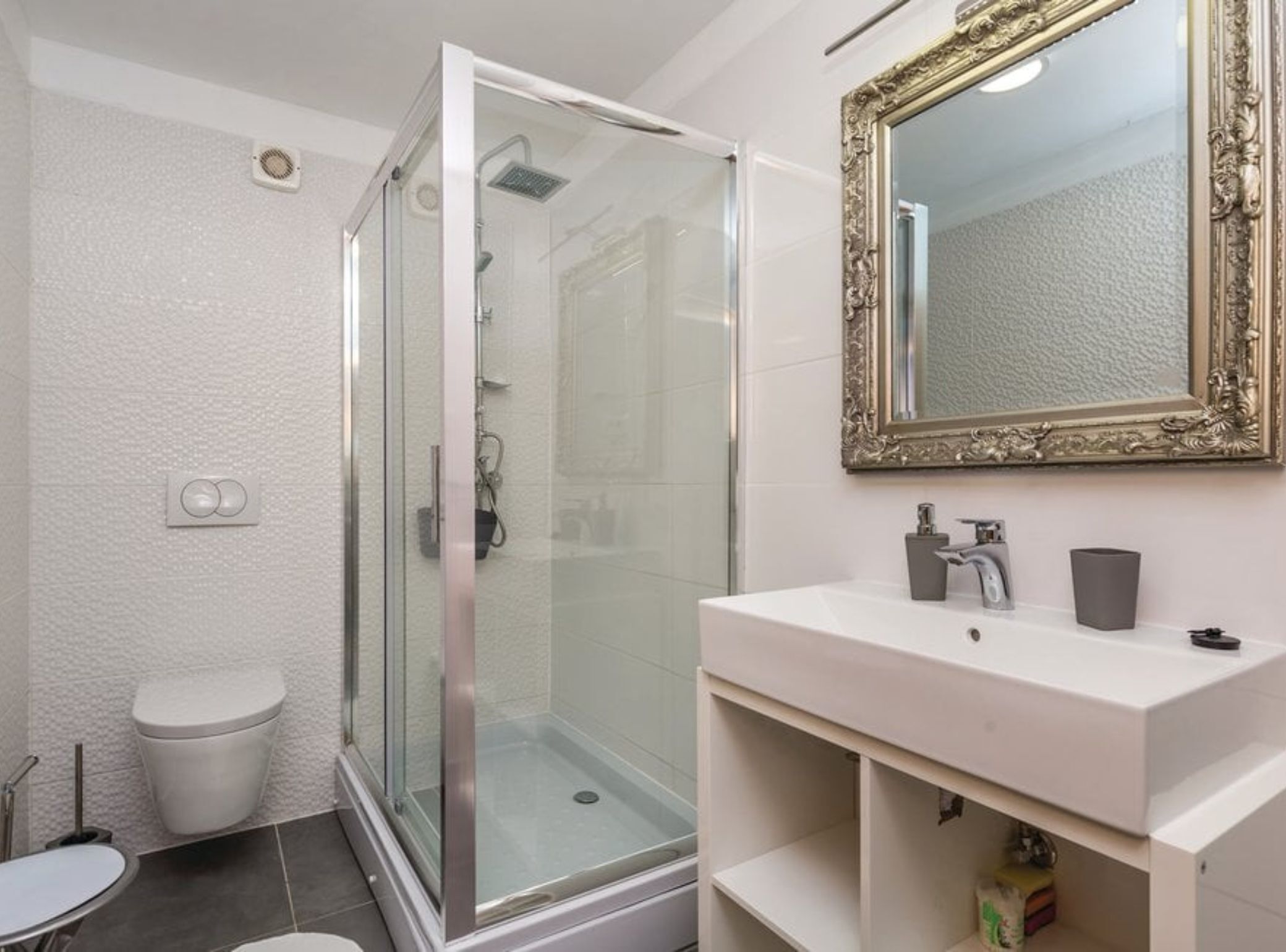 A modern bathroom with a glass-enclosed shower, a white sink with a mirror, and a toilet.