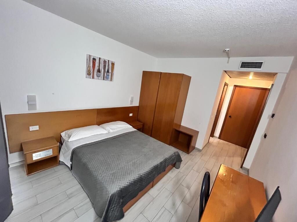 Un dormitorio con cama, armario de madera, mesita de noche y un escritorio pequeño con silla.
