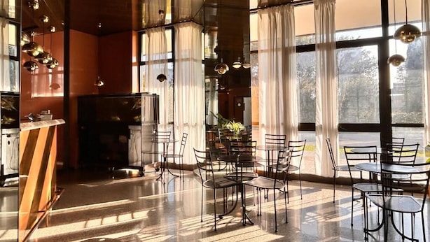 A spacious indoor area with large windows, tables, chairs, and hanging pendant lights.