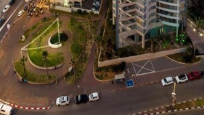 Um edifício alto com vários andares, uma rotatória e uma praia ao fundo.