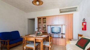 Un salon comprenant une table à manger en bois, des chaises, un canapé bleu, un canapé blanc, un téléviseur et un meuble en bois.