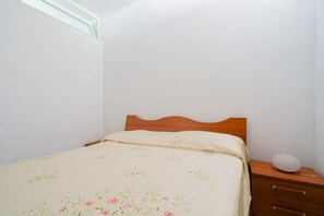 Een slaapkamer met een eenpersoonsbed, een houten hoofdbord, een nachtkastje met een lamp en een raam.