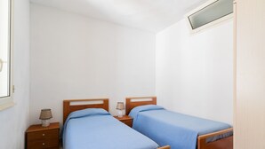 Une chambre à coucher avec deux lits en bois, une table de chevet avec une lampe et une fenêtre donnant sur le ciel.