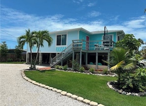 A two-story house with a balcony, a front porch, and a small garden with palm trees. - The Blue Retreat (Fort Myers Beach)
