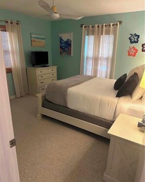 A bedroom with a bed, a nightstand, a dresser, a ceiling fan, and a window with curtains. - The Blue Retreat (Fort Myers Beach)