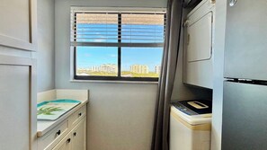 A compact kitchen with a window, a washing machine, and a refrigerator. - Beach Watch (Bonita Springs)