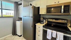 A compact kitchen with a refrigerator, microwave, oven, and a small countertop with a toaster. - Beach Watch (Bonita Springs)