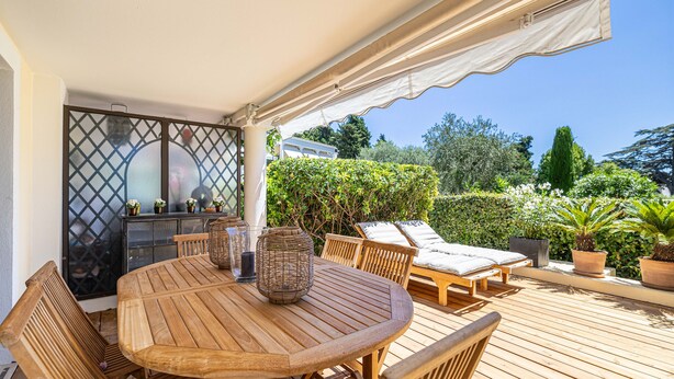 A wooden deck with a round table and chairs, a covered seating area, and potted plants. - Le Paradis avec deux terrasses équipées et piscine (Cannes)