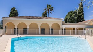 A swimming pool with a tiled deck, surrounded by a building with arched windows and a tiled roof. - Le Paradis avec deux terrasses équipées et piscine (Cannes)
