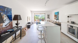 A modern kitchen with white cabinetry, a central island with bar stools, and a dining area with a sofa and chairs. - Le Paradis avec deux terrasses équipées et piscine (Cannes)