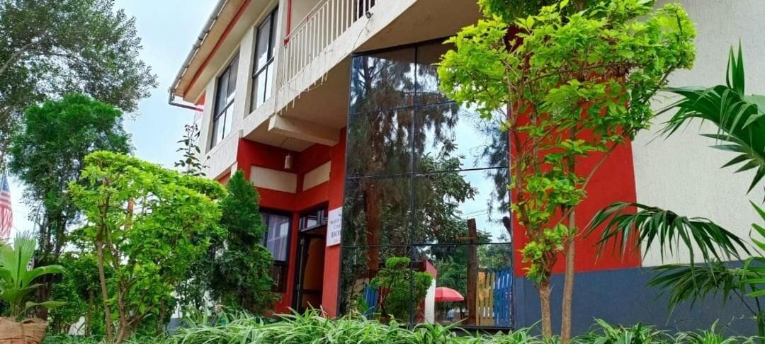 A building with a red and white facade, a balcony, and lush greenery in the foreground.