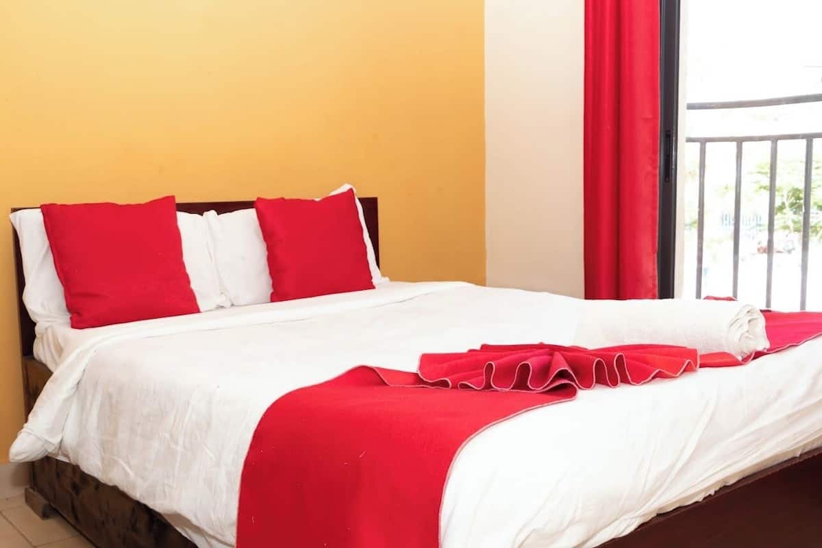 A bed with white and red bedding, a wooden headboard, and a balcony with a red curtain.