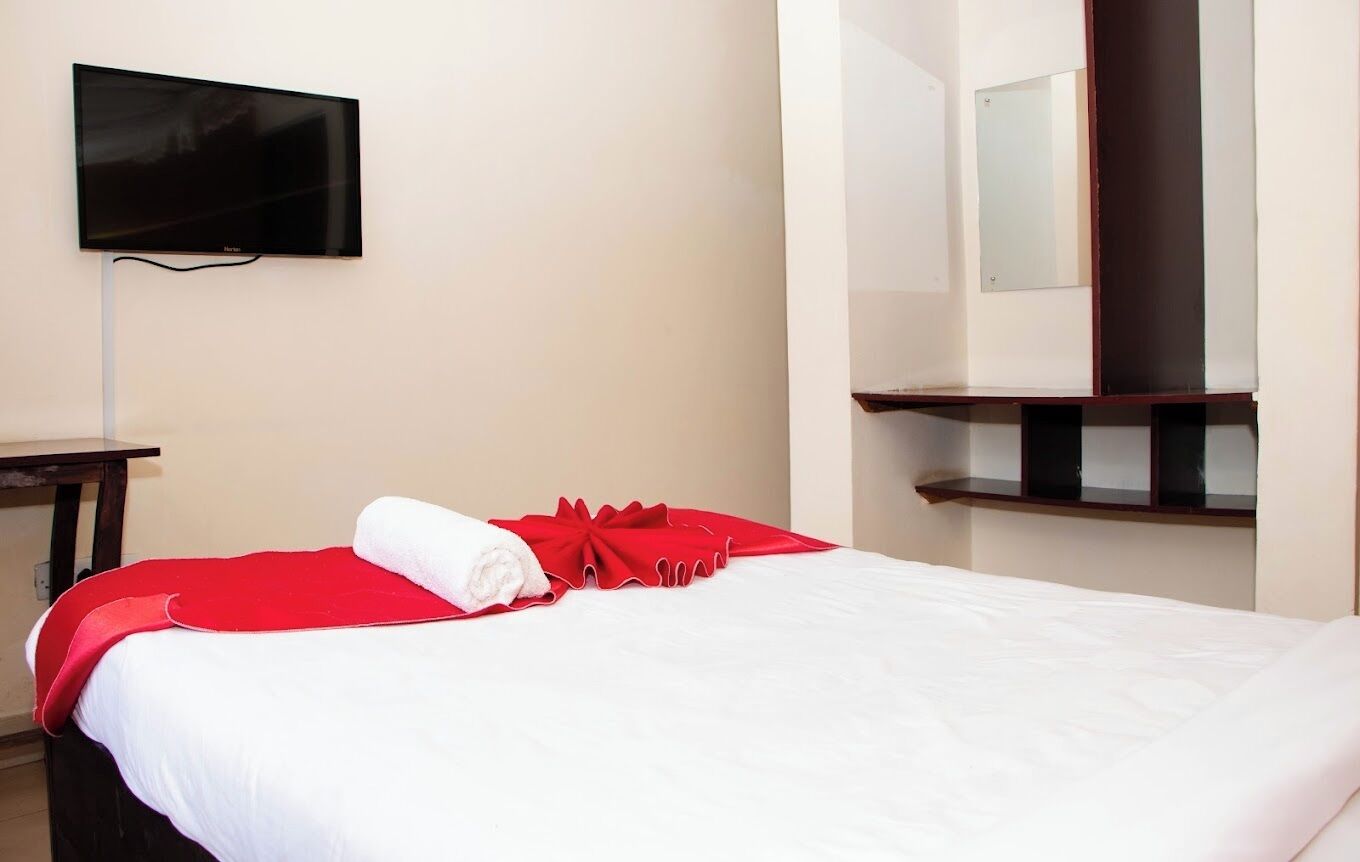 A hotel room with a bed, a TV mounted on the wall, a mirror, and a small table.
